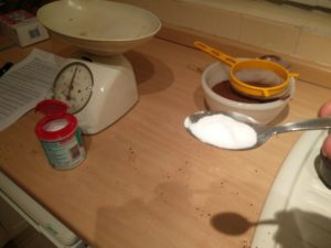 Baking powder on a teaspoon, with the packet and coca flour mix in the background