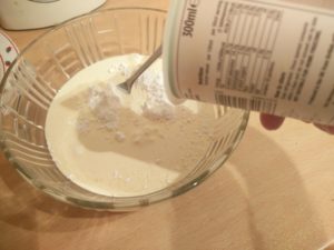 Sugar in a mixing bowl with a carton of cream being poured onto it